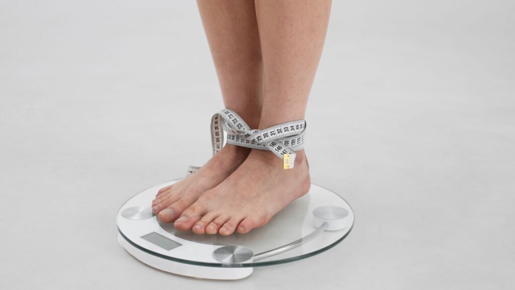 pessoa se pesando em uma balança, amarrada a uma fita metrica