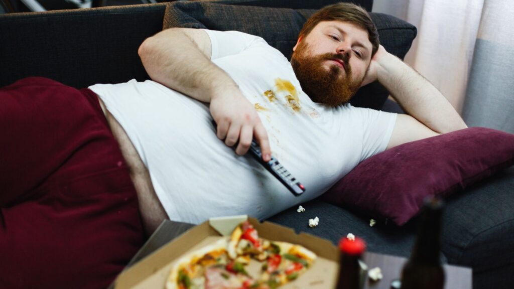 Homem acima do peso deitado no sofá assistindo TV