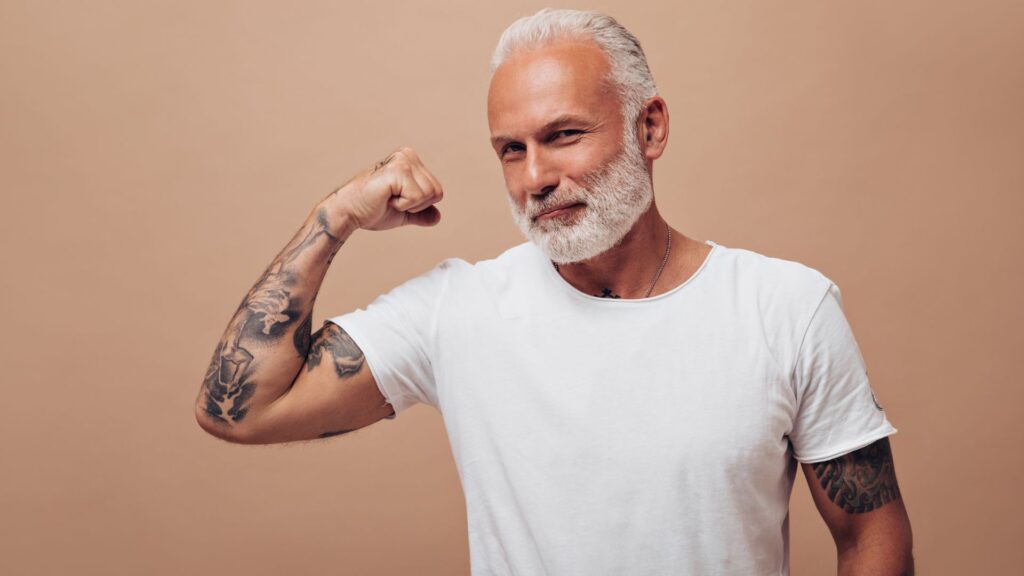 Homem mais velho de branco mostrando músculos em fundo bege