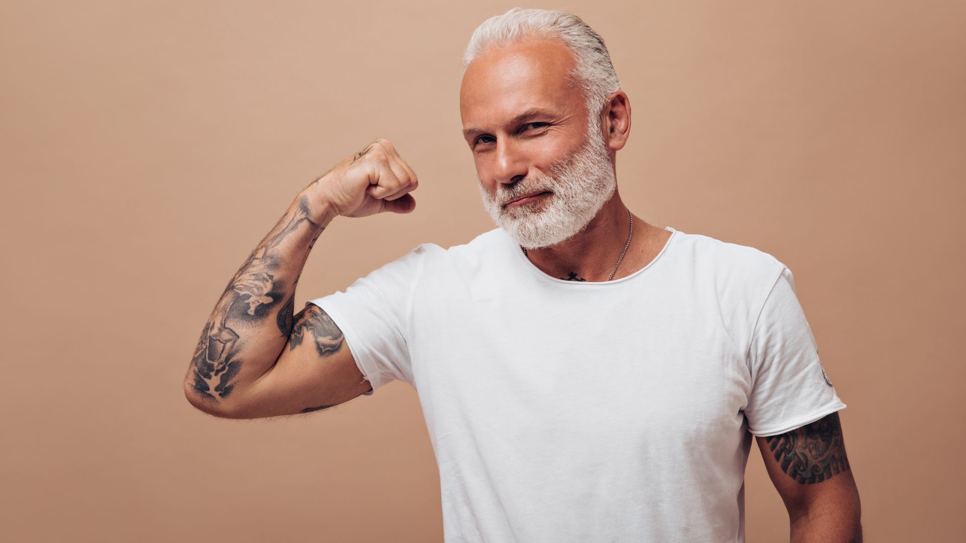 Homem mais velho de branco mostrando músculos em fundo bege