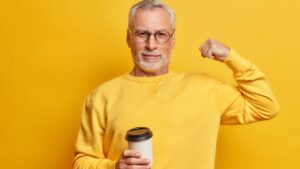 Homem mostrando bíceps com copo de café em fundo amarelo